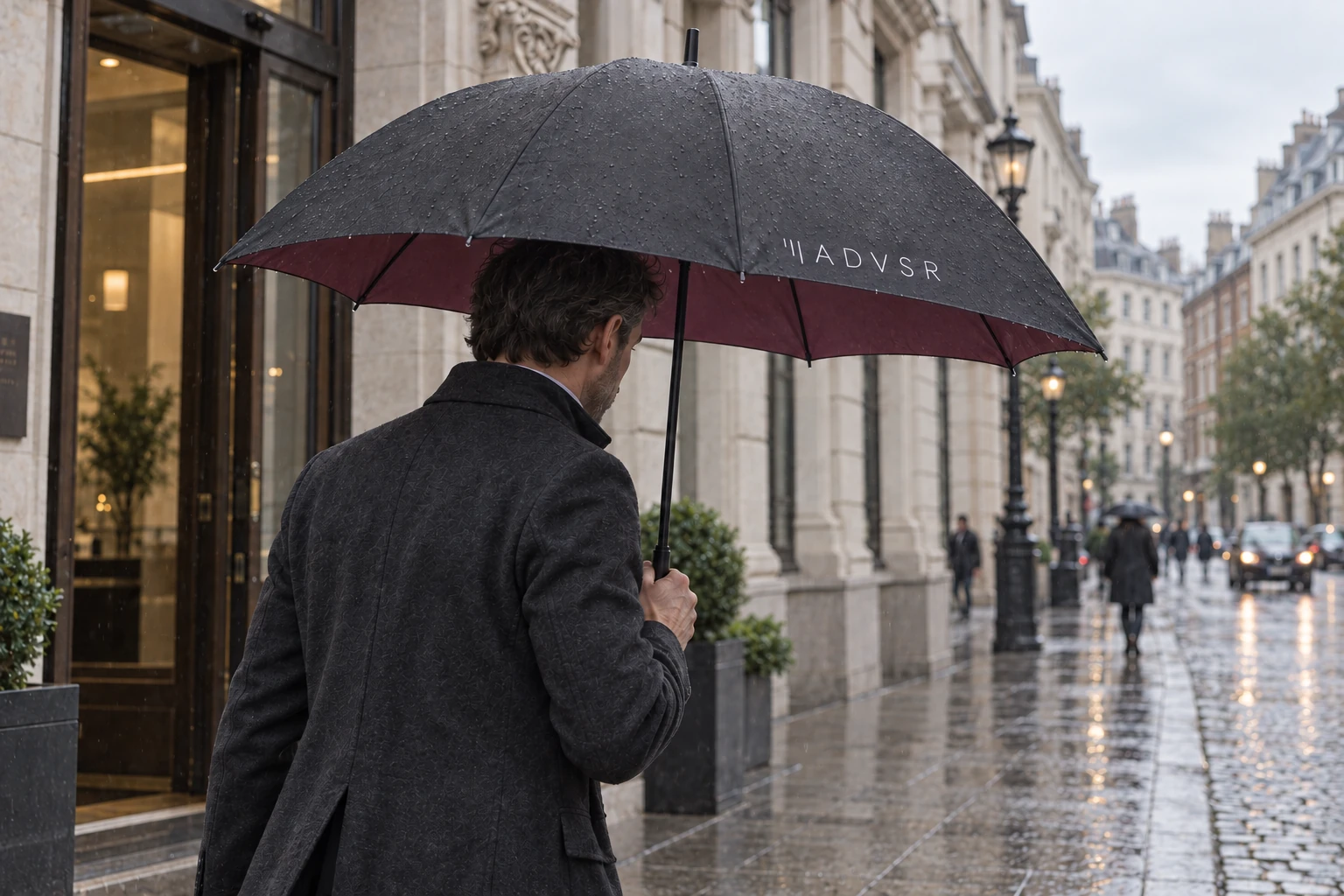 A person walks along a wet city street under a graphite ADVSR umbrella with a wine-coloured lining.